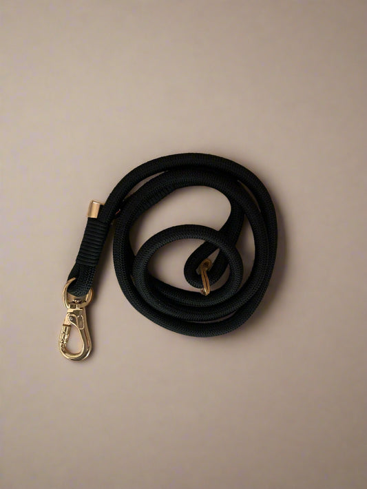Black dog leash with a gold clasp on a light wooden surface