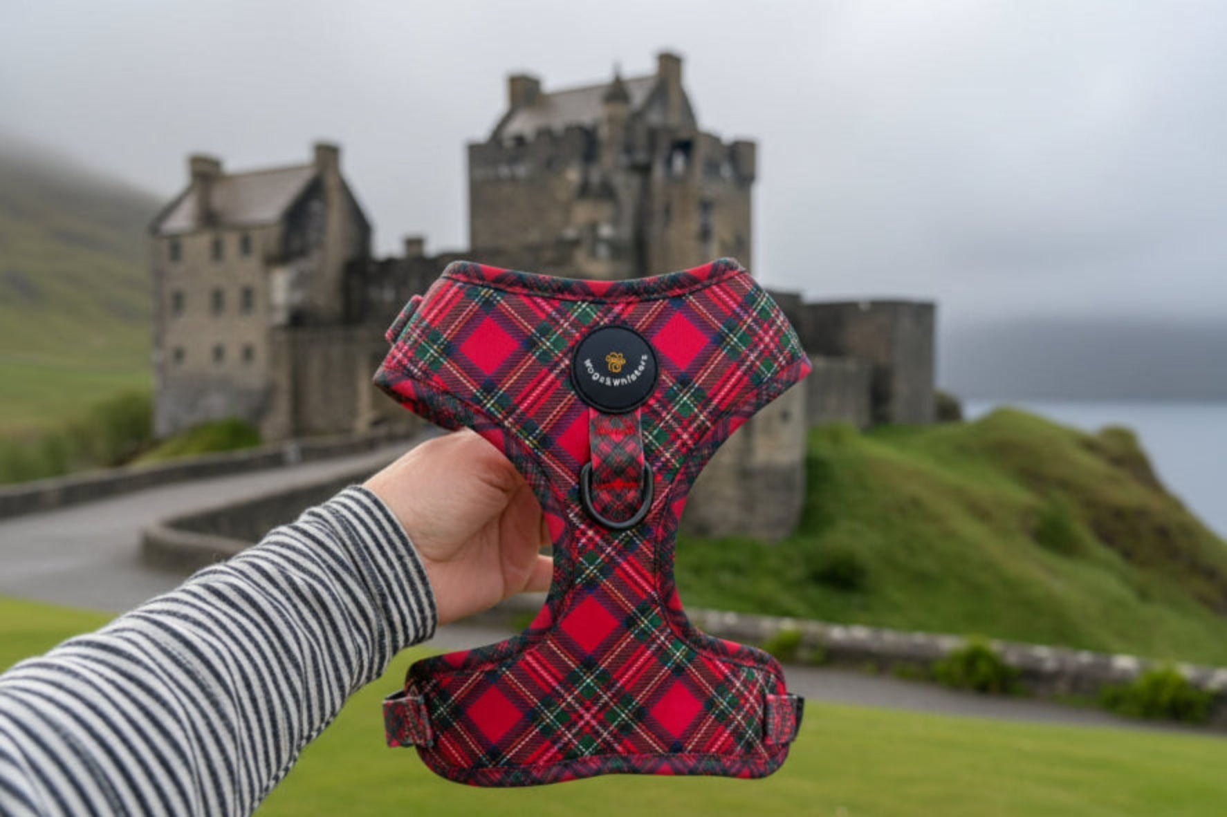 Red plaid dog harness held by a person with a blurred castle background