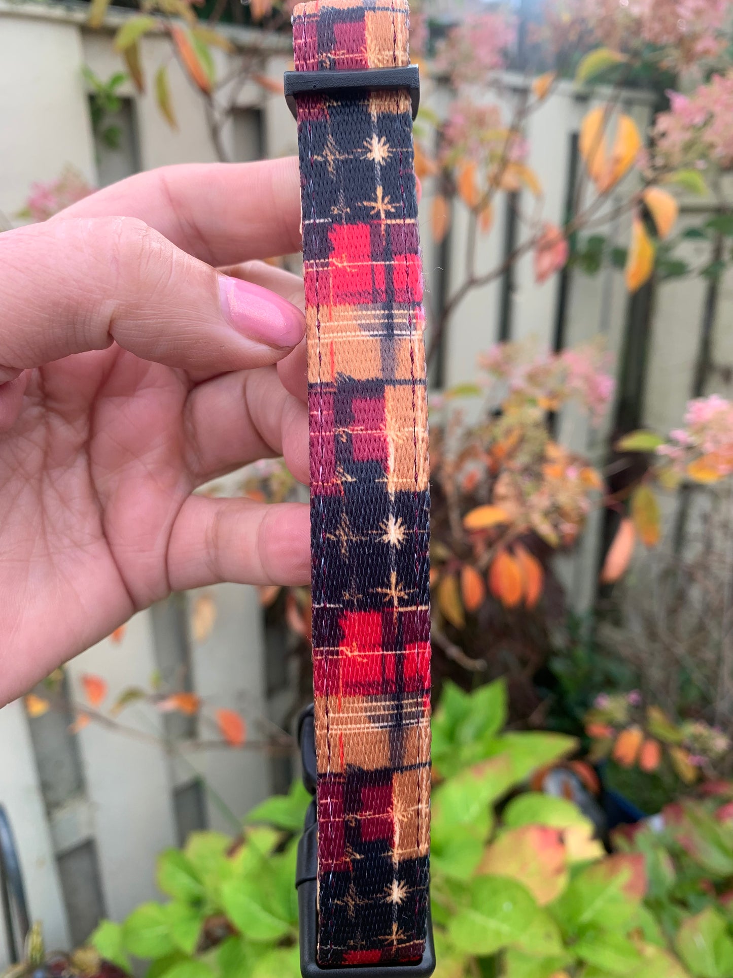 Plaid-patterned belt held by a hand with a blurred outdoor background